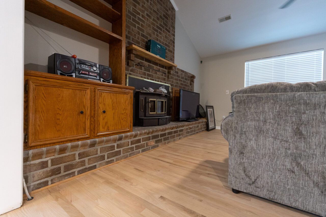 Lived-in family room with new light red oak flooring running up to a brick hearth, built-in wood cabinets and a gray sofa