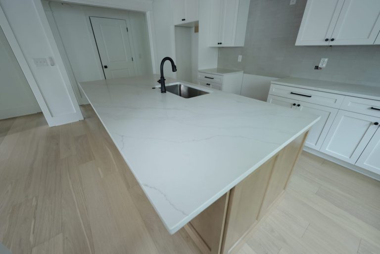 Renovated kitchen with a white quartz-topped island, undermount sink and black faucet, white shaker cabinets and light oak floors