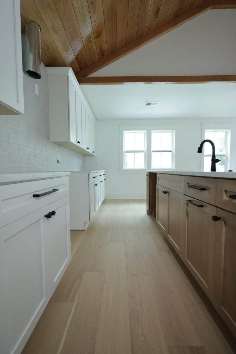 Cathedral Ceilings: What a Charleston Builder Settles Before the Boards Go Up Galley kitchen under a sloped cypress board ceiling, with a stained beam where it meets the flat white ceiling and a stainless range hood chimney rising into the slope