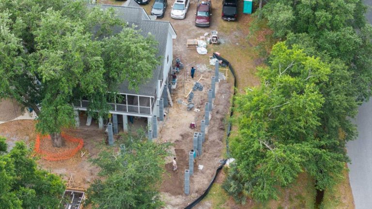 Aerial view of new concrete block columns lined up beside a raised house with a screened porch, under live oaks, for an addition in Mount Pleasant
