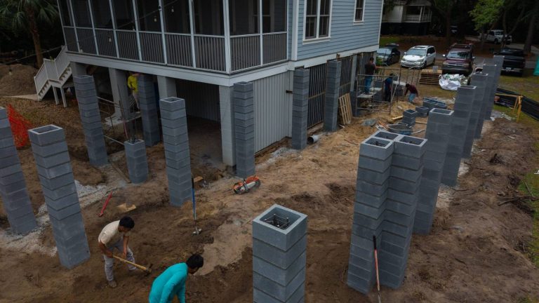 Aerial view of concrete block columns for a home addition beside a raised house with a screened porch